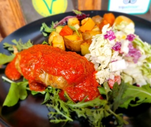 Zdjęcie przedstawia talerz, na nim gołąbeki z mięsem z grochu podane z sosem pomidorowym, pieczonymi ziemniakami i surówką