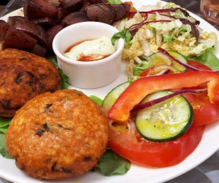 Zdjęcie przedstawia potrawę Kotlety z kaszy jaglanej i pokrzywy z pieczonymi ziemniakami, surówką, warzywami i sosami